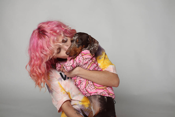 A girl with pink hair is smiling with a dog. friends Marble dachshund. White background - Foto, afbeelding