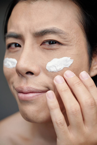 Face of smiling man applying brightening moisturizer on face after shower - Foto, imagen