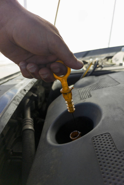 Hombre comprobando su nivel de aceite del viejo motor diesel. Fondo de gasolinera - Foto, imagen