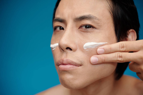 Gesicht des ernsthaften Mannes Anwendung Aufhellung Feuchtigkeitscreme auf Gesicht - Foto, Bild