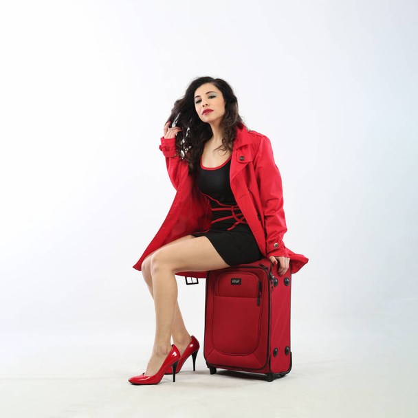 Beautiful young brunette woman in a red coat with a suitcase - Fotó, kép