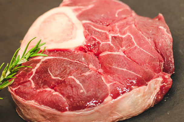 Pedaço fresco de carne bife grande carne no osso ossobuco com um raminho de alecrim em um fundo preto. - Foto, Imagem