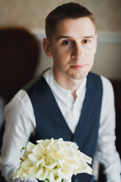 Beautiful man, groom holding big and beautiful wedding bouquet with flowers. - Zdjęcie, obraz