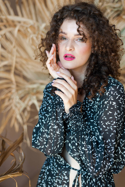 beautiful young woman with curly hair in a black dress and a scarf on a background of a wooden wall - Photo, Image