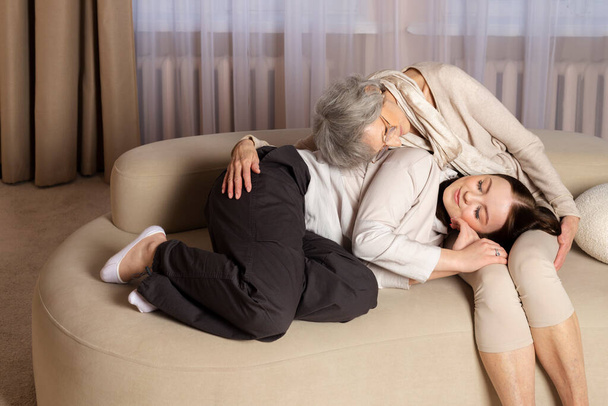 Una abuela o anciana y una nieta o niña están teniendo una conversación dulce y amistosa mientras están sentadas en un sofá. Familia fuerte, amorosa y feliz. - Foto, imagen
