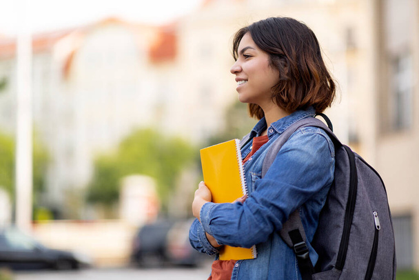 College Student. Happy Young Arab Woman With Backpack And Workbooks Standing Outdoors At Campus, Smiling Middle Eastern Female Resting Outside After Classes, Side View With Copy Space - Foto, afbeelding