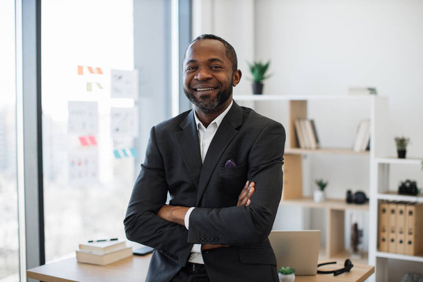 Close up of successful businessman in formal attire smiling at camera while working in modern work environment. Cheerful african american executive manager enjoying his work-life balance at office. - Фото, зображення