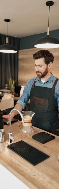Handsome barista wearing apron grinds coffee beans in coffeemachine - Fotoğraf, Görsel