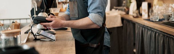 Smiling barista holding payment terminal while standing behind counter - Photo, Image