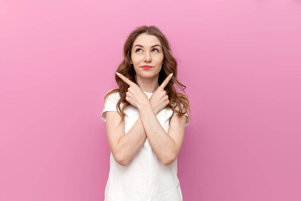 young cute woman chooses from two options and shows with her hands to both sides on pink isolated background, thoughtful girl puzzled by difficult choice - Foto, immagini