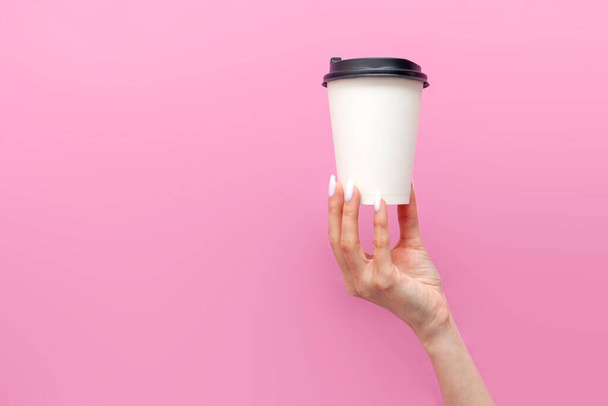 white blank paper cup of coffee in the hands of woman on pink isolated background, the girl's hands hold disposable cardboard cup with drink and advertise copy space - Photo, Image