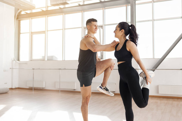beautiful athletic couple in sportswear warm up in the gym in the morning, fitness girl and coach man go in for sports in training in bright room - Photo, Image