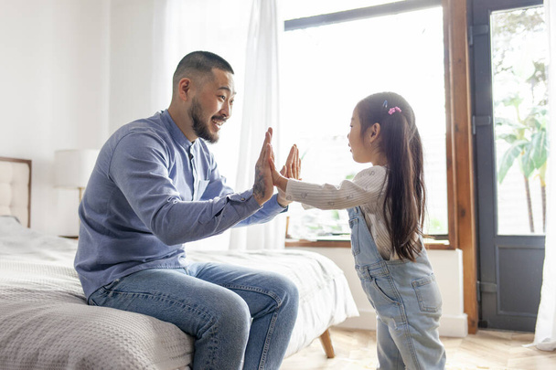 little Asian girl screams and plays with her dad in her hands, Korean child gives five to her father at home, man educates and plays with her daughter in the room - Photo, Image