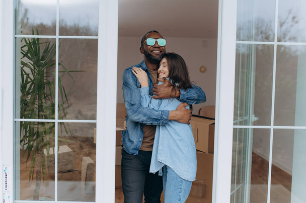 Счастливый молодой человек обнимает взволнованную жену, празднуя день переезда с картонными коробками, арендаторов - Фото, изображение