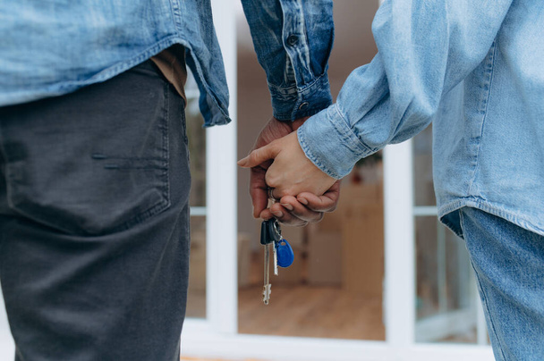 Closeup of young couple holding hands and new house key. Mortgage, real estate concept - Photo, Image