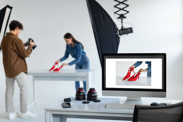 Zespół profesjonalistów, fotograf i jego asystent pracujący i robiący zdjęcia butów w photostudio, selektywne skupienie się na monitorze z nową treścią zdjęcia - Zdjęcie, obraz