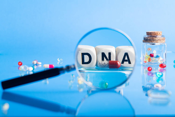 Laboratuvar masasının arka planında ilaç ve hazırlıklarla birlikte DNA hapları. Büyüteçle bak. Mavi arka planda. Seçici odak. - Fotoğraf, Görsel
