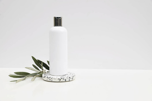 Cosmetic product mockup on white background. Plastic pump bottle for shampoo, lotion template. Stone terrazzo podium.Green olive tree branch. Healthy cosmetology, spa treatment concept, copyspace - Fotografie, Obrázek