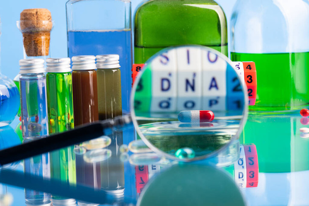 DNA pill on the background of a laboratory table with medicines and preparations. View through a magnifying glass. On a blue background. Selective focus. - Photo, image