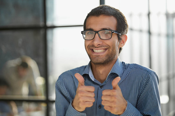 Young businessman in casual wear approves positive hand gesture, smiles and rejoices in success. winner gesture. - Foto, afbeelding