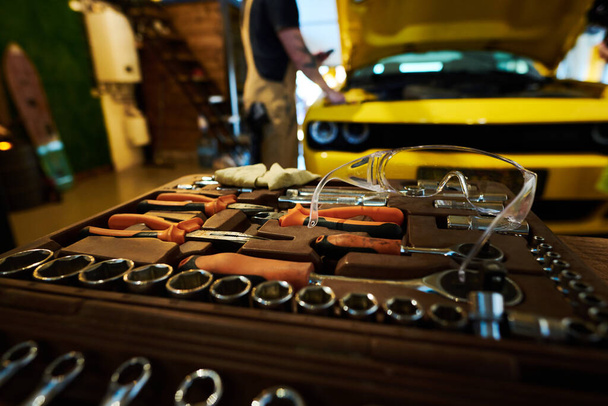 Gafas protectoras en la parte superior del kit con piezas de repuesto y herramientas manuales para trabajos de reparación y chequeo de automóviles contra reparador - Foto, Imagen