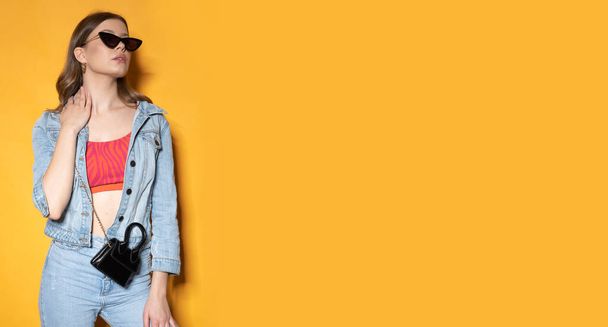 Модна молода жінка з чорними сонцезахисницями на жовтому тлі. Сильний світловий знімок
. - Фото, зображення