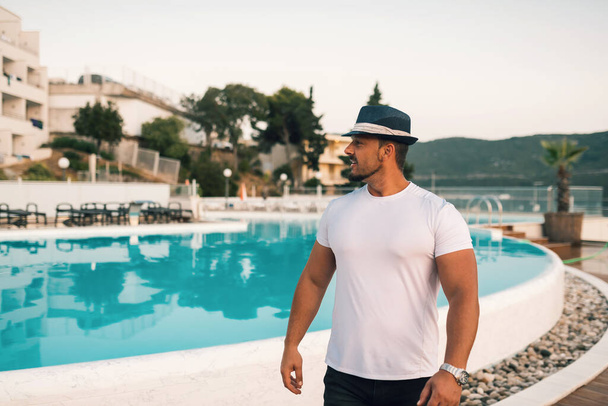Un uomo in forma e attraente in vacanza in un hotel vicino a una spiaggia di sabbia. Indossa un cappello elegante e gode del caldo sole e del mare cristallino. Il paesaggio è sereno e idilliaco, che ritrae un senso - Foto, immagini