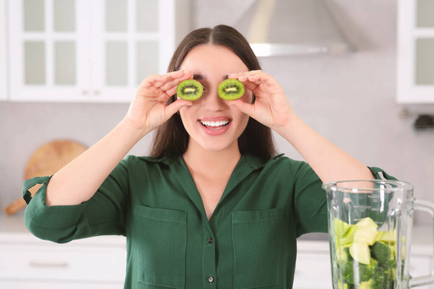 Young woman with cut kiwi for smoothie in kitchen - Foto, Imagem
