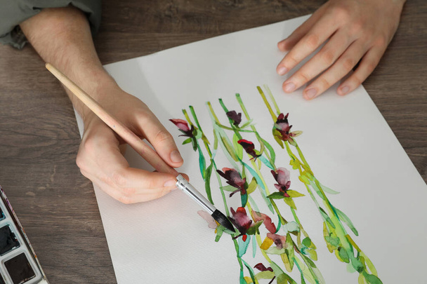 Man painting flowers with watercolor at wooden table, closeup. Creative artwork - Fotoğraf, Görsel