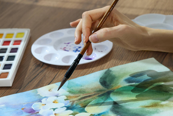 Woman painting flowers with watercolor at wooden table, closeup. Creative artwork - Foto, Bild