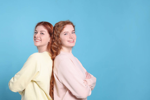 Portrait of beautiful young redhead sisters on light blue background. Space for text - Fotó, kép