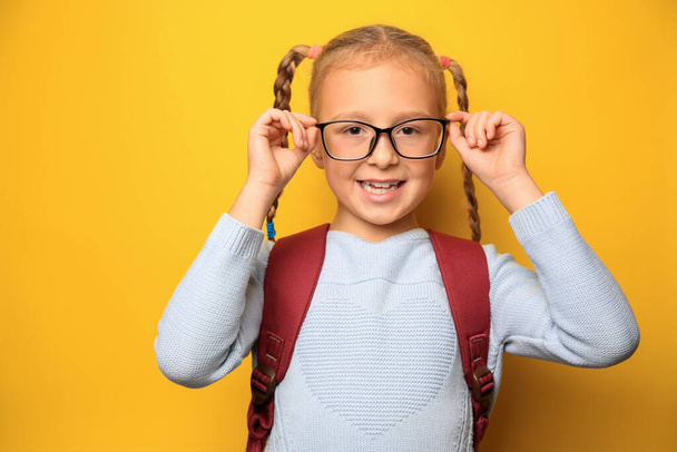 Cute little girl with backpack wearing glasses on yellow background - Zdjęcie, obraz