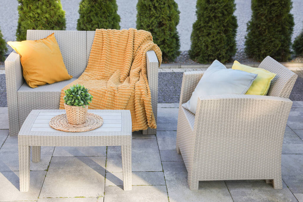 Beautiful rattan garden furniture, soft pillows, blanket and houseplant outdoors - Foto, Imagen