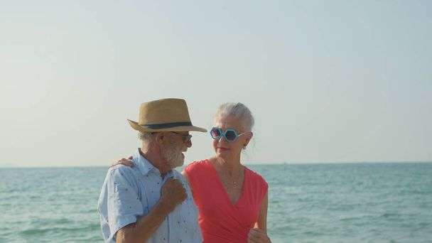 Egy idős pár átöleli a vállát a tengerparton a nyári vakációjukon, mosolyognak és élvezik a vakációt.. - Fotó, kép