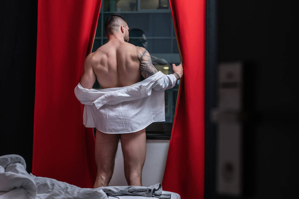 Man with naked body, muscular shoulders. Naked man in bed. Muscular sexy male body. Gay sexy model. Muscular sexy man with naked torso near window curtains. Hunk with athletic body. Guy enjoying night - Fotografie, Obrázek