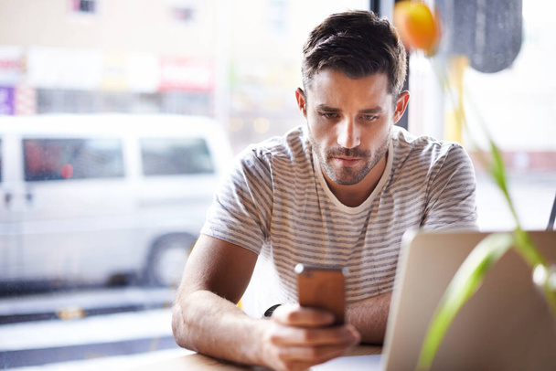 Проверяю дважды. молодой человек пишет смс на свой телефон и использует ноутбук в кафе - Фото, изображение