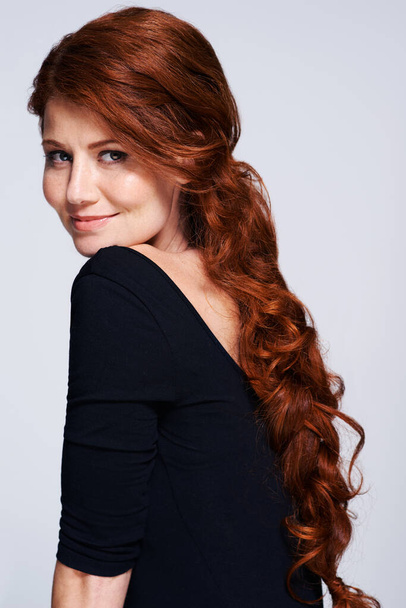 Its more than just hair, its an attitude. Studio shot of a young woman with beautiful red hair posing against a gray background - Foto, afbeelding