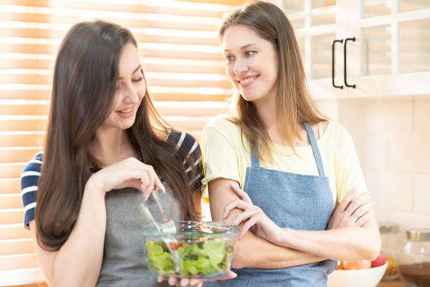 glücklich und lächelnd lesbisches Paar, das in der Küche Salat kocht. Salat in Glasschüssel mit süßem Lächeln beim gemeinsamen Kochen. Stolzer Monat zur Förderung von Gleichberechtigung und Unterschieden zwischen Homosexuellen. - Foto, Bild