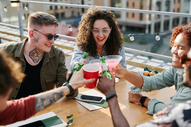 Onnellinen nuori rotujenvälinen ystäviä clinking heidän juomia yli pöydän ulkona kahvilassa nauttien katolla osapuoli viikonloppuna - Valokuva, kuva