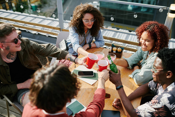 П'ять веселих молодих друзів чіпляються зі своїми напоями за стіл, відпочиваючи у відкритому кафе в сонячний літній день
 - Фото, зображення