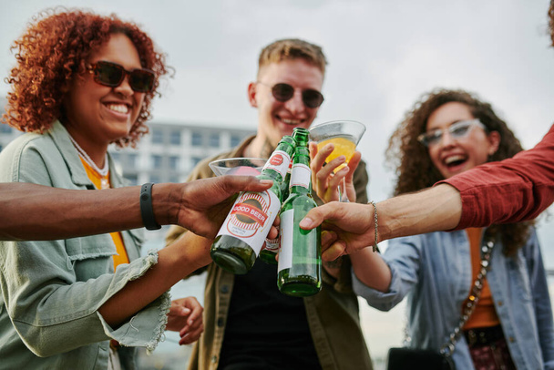 Bir grup mutlu, çok kültürlü insan çatıdaki kafede toplanırken bir yandan bira ve kokteyl şişeleriyle çakışıyor. - Fotoğraf, Görsel