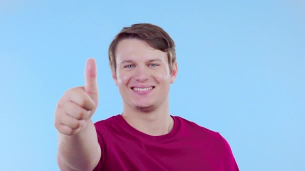 Face, support and man with thumbs up, smile and agreement against blue studio background. Portrait, male person or guy with symbol for solidarity, ok and like with gesture for well done and promotion. - Footage, Video