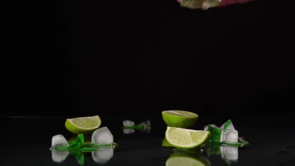 Un primo piano della mano del barista Raccogliere un bicchiere di Mojito sul tavolo con lime, rum e foglie di menta verde su sfondo nero - Filmati, video