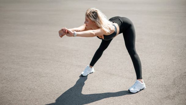 Sporty woman stretching and warming up legs for running urban fitness workout. Sport and healthy lifestyle concept. Female athlete exercising outside - 写真・画像