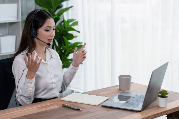 Asian call center with headset and microphone working on her laptop. Female operator provide exceptional customer service. Supportive call center agent helping customer on inquiry. Enthusiastic - Valokuva, kuva