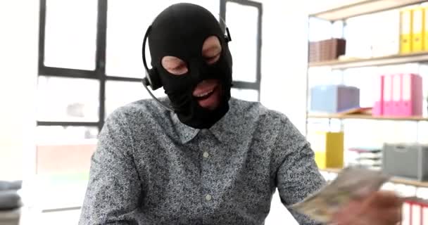 Internet scammer in balaclava with headphones with microphone counting money in front of laptop 4k movie. Cheating and theft online concept - Footage, Video