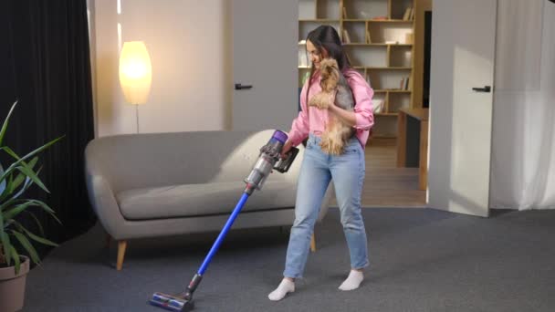 Woman with vacuum cleaner and dog in her hand vacuuming in the living room. - Footage, Video