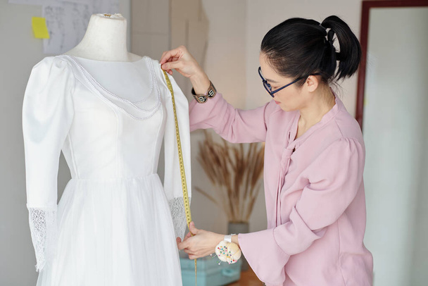 Швея измеряет рукава белого платья на манекене - Фото, изображение
