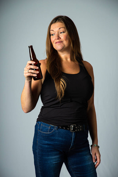 Isolated forty year old woman wearing a black tank top, holding a brown beer bottle - Фото, изображение