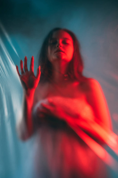 Mental disorder. Art portrait. Emotional crisis. Red blue color light defocused disturbed desperate woman silhouette touching transparent polyethylene plastic wall. - Fotografie, Obrázek